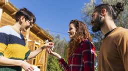 A smiling woman in glasses hands over the keys to a happy couple.